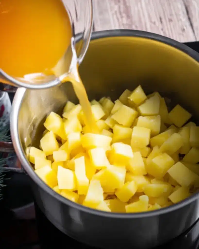 Pouring chicken broth over diced potatoes in a soup pot