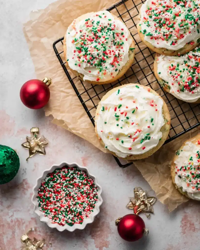 Christmas sprinkle cookies with frosting on a wire rack and festive decorations