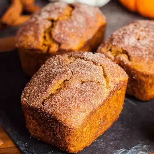 Mini cinnamon swirl pumpkin bread loaves with sugar topping on a dark board