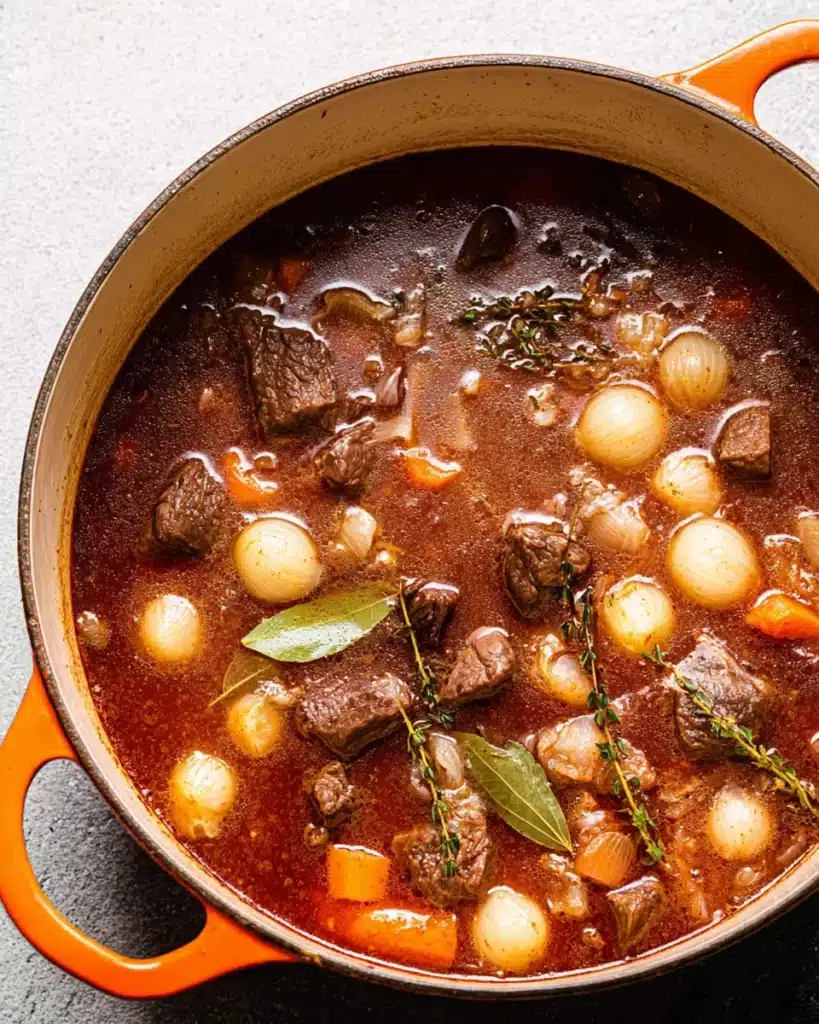 Classic Beef Bourguignon (Christmas Recipe) 5 Beef bourguignon simmering with pearl onions, carrots, and herbs in Dutch oven