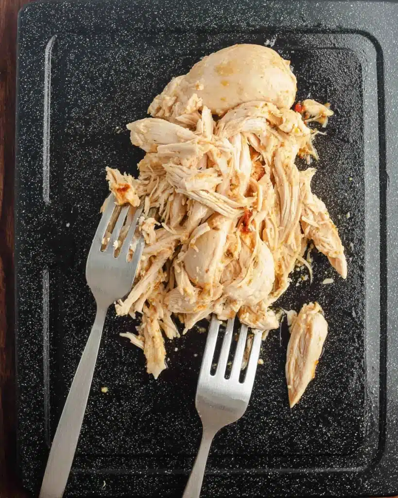 Shredding cooked chicken with forks for CrockPot Cheesy Chicken Spaghetti