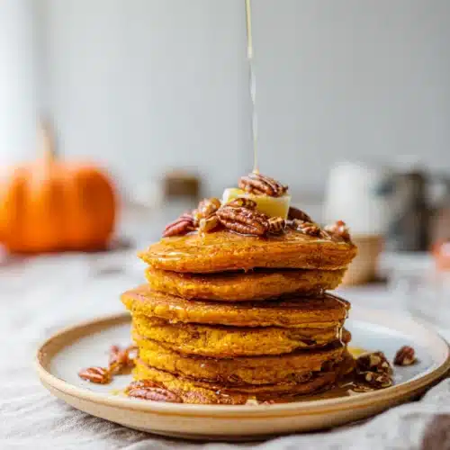 Fluffy pumpkin pancakes with maple syrup and pecans on a plate
