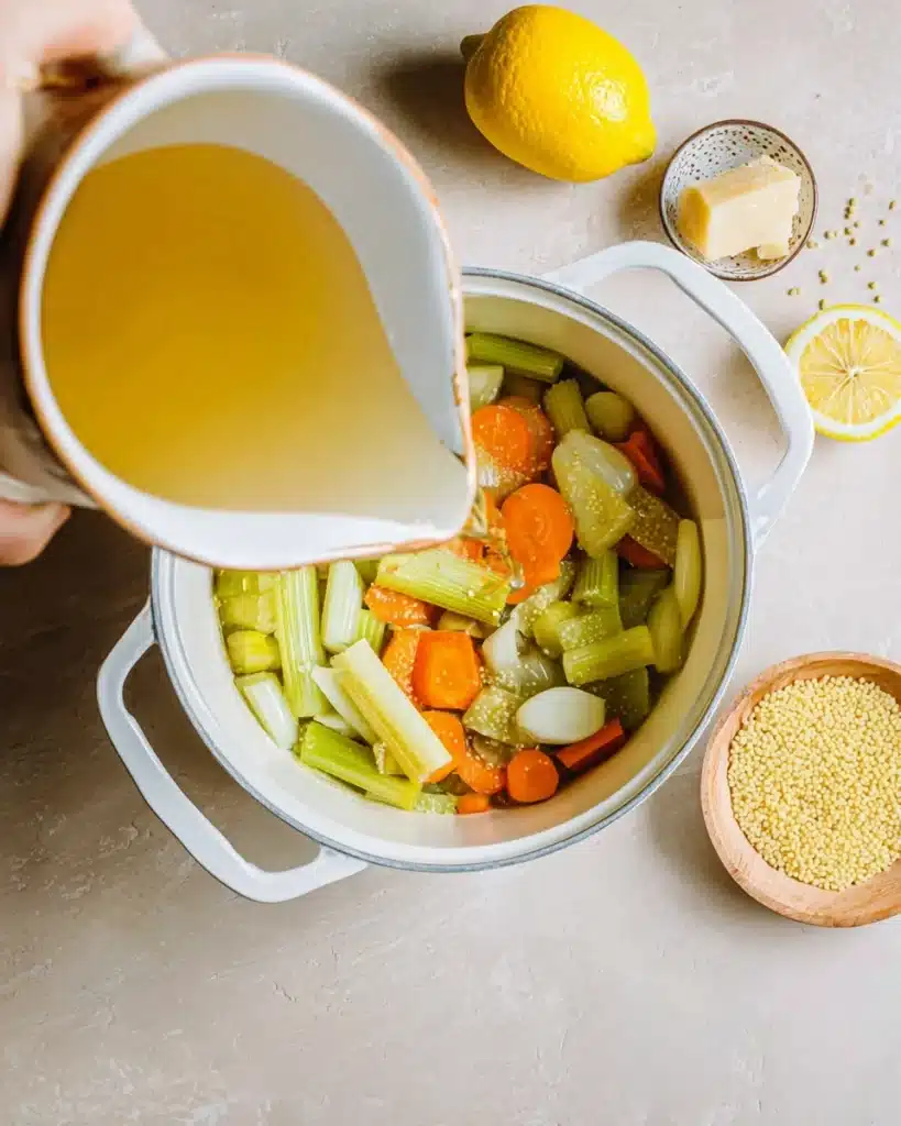 Italian Penicillin Soup Recipe 3 Pouring golden broth over sautéed vegetables in a white pot for Italian penicillin soup