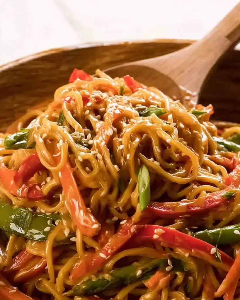 Close-up noodle salad with sesame peanut dressing, glossy noodles, and fresh vegetables.
