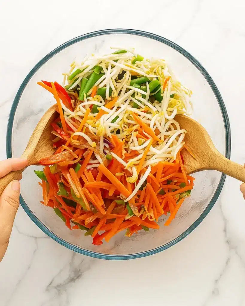 Sesame peanut dressing poured over fresh vegetables and noodles in a bowl.