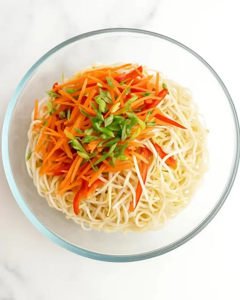 Fresh vegetables and noodles in a glass bowl for sesame peanut noodle salad.