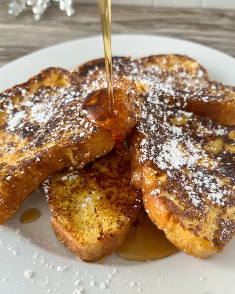 Pumpkin French Toast slices with powdered sugar and maple syrup on a white plate