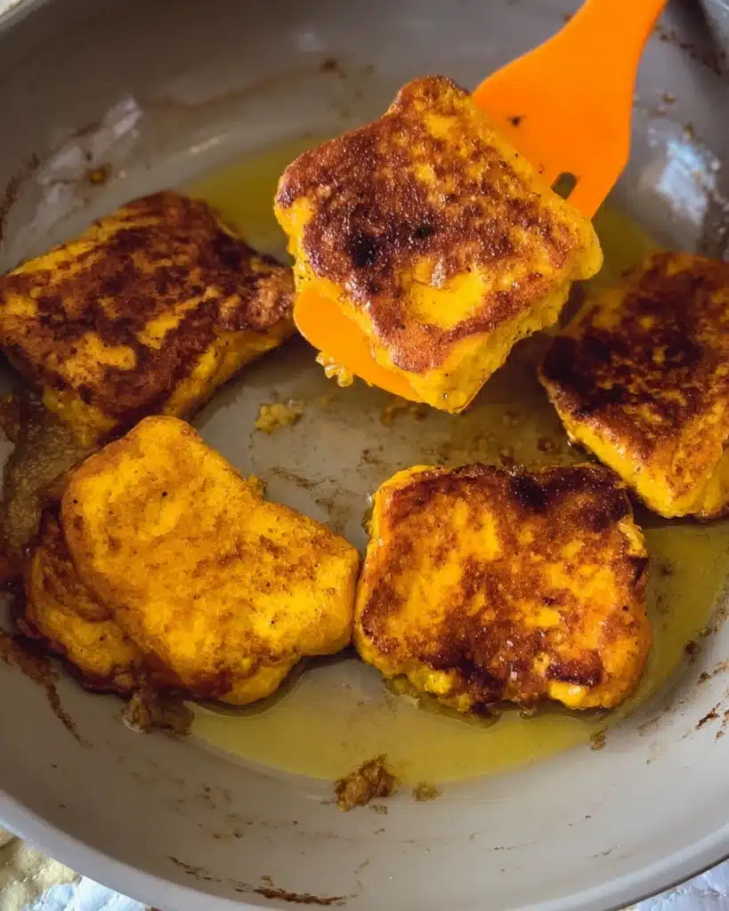 Pumpkin French Toast slices cooking in a skillet with spatula