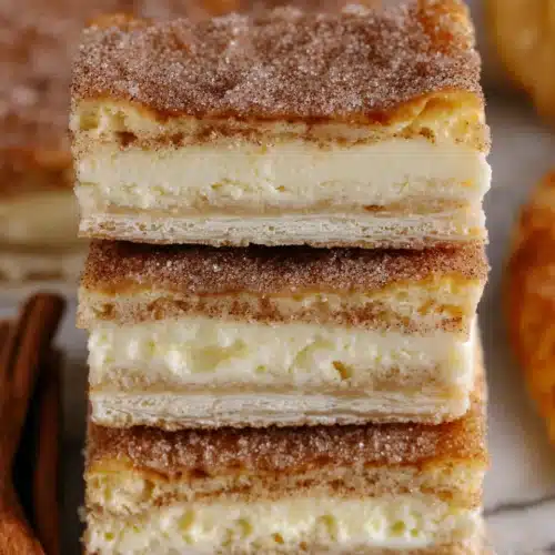 Stacked churro cheesecake bars with flaky crust, creamy filling, and cinnamon sugar topping