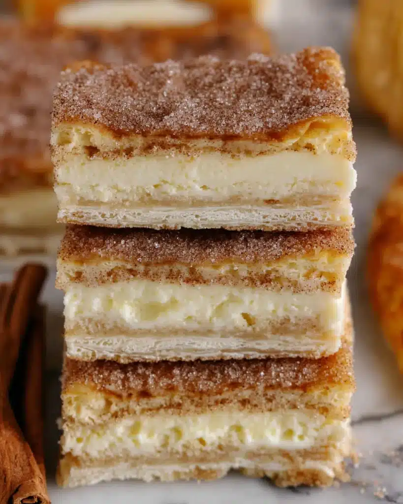 Stacked churro cheesecake bars with flaky crust, creamy filling, and cinnamon sugar topping