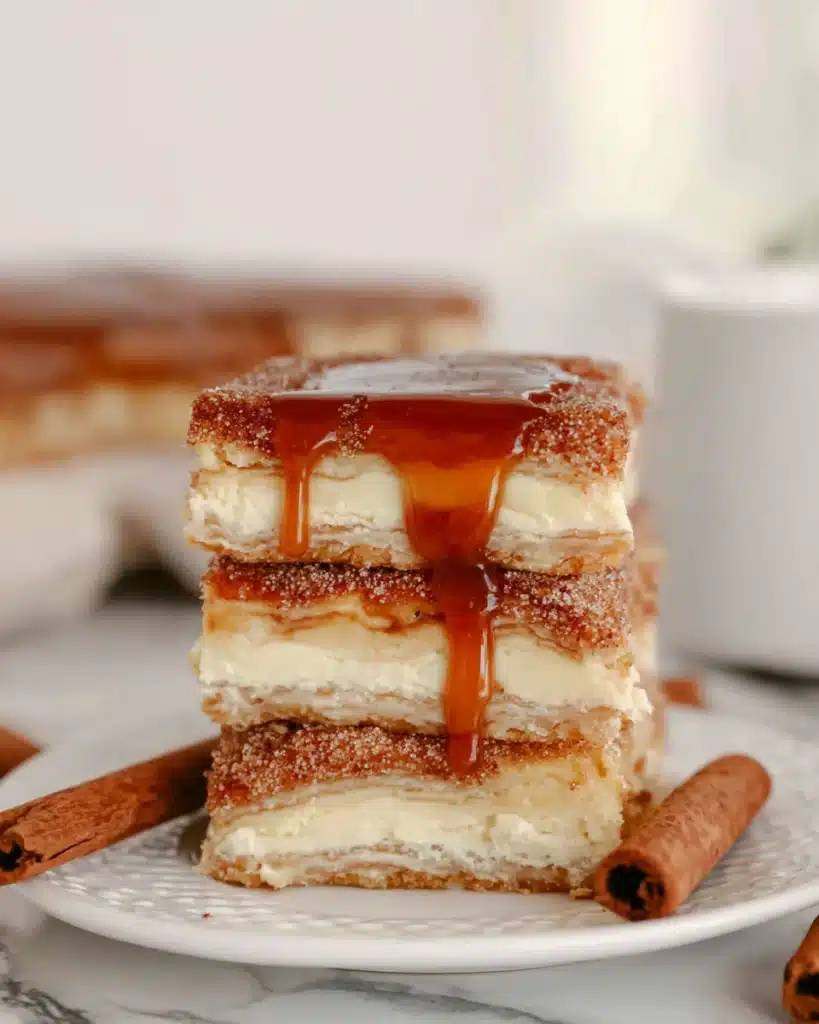 Simple churro cheesecake bars drizzled with caramel sauce on a white plate