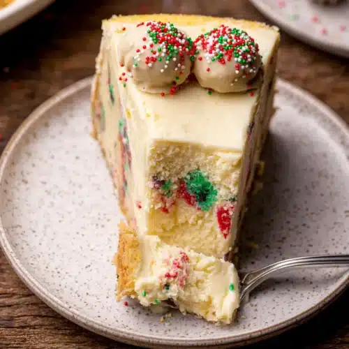 Slice of sugar cookie cheesecake with sprinkles on plate