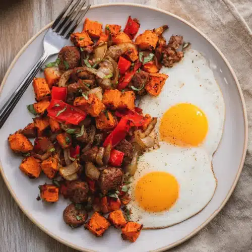 Sweet Potato Breakfast Hash (Thanksgiving Recipe) 6 Sweet potato breakfast hash with sausage, peppers, and sunny-side-up eggs on a plate