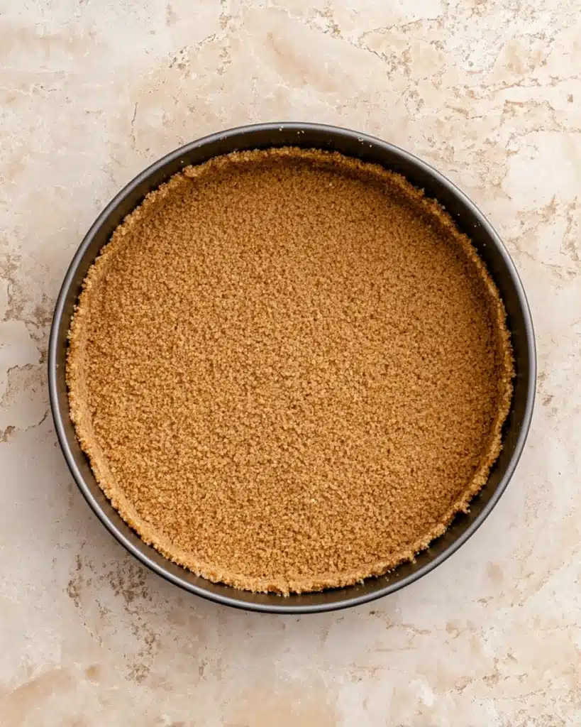 Golden graham cracker crust pressed into springform pan for cheesecake