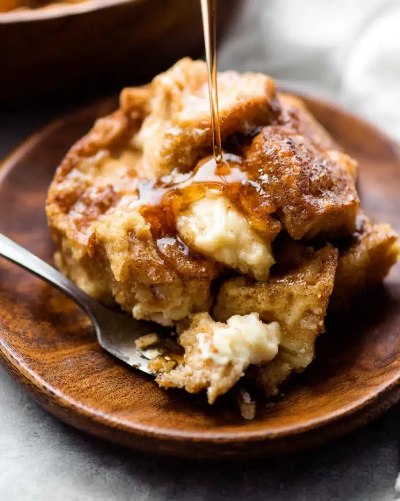 Slice of baked cream cheese French toast casserole with maple syrup on wooden plate