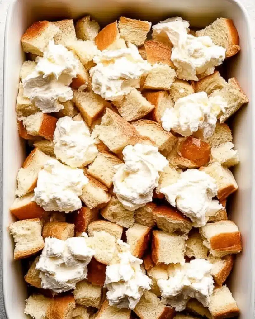 Layered bread cubes and cream cheese in baking dish for French toast casserole