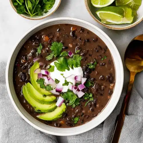 Black Bean Soup 6 Hearty black bean soup topped with avocado, red onion, cilantro, and sour cream in a ceramic bowl