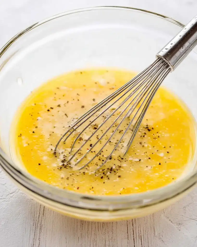 Breakfast Sandwiches: Easy, Freezer-Friendly Morning Meal 5 whisking eggs with black pepper in glass bowl for breakfast sandwiches
