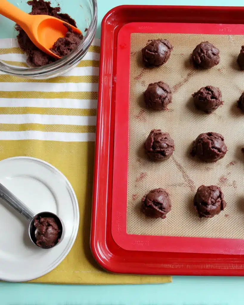 Cake Mix Cookies – The Easiest 3-Ingredient Dessert Ever! 3 Chocolate cookie dough scoops on baking sheet with spatula and cookie scoop