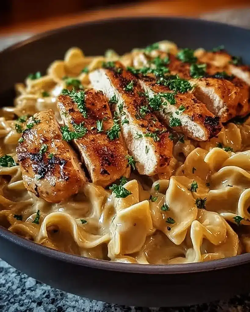 Chicken with Buttered Noodles Recipe 2 Grilled chicken served on creamy buttered noodles, garnished with parsley in a dark bowl.