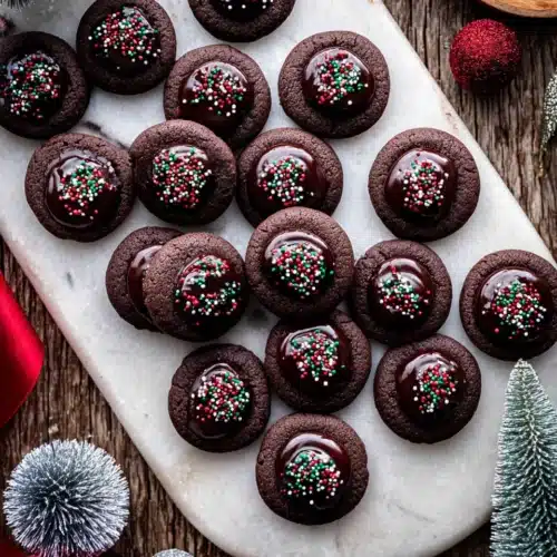 Chocolate Thumbprint Cookies 11 Chocolate thumbprint cookies with glossy ganache and festive sprinkles on a marble board