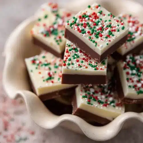 Christmas Fudge Recipe 8 Christmas Fudge Recipe squares with white chocolate and festive sprinkles in a ceramic dish