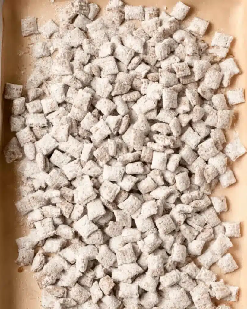 Christmas Puppy Chow (Festive Muddy Buddies) 4 Powdered sugar-coated Chex cereal on parchment for Christmas Puppy Chow