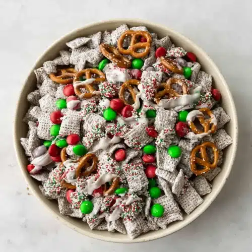 Christmas Puppy Chow (Festive Muddy Buddies) 7 Christmas Puppy Chow snack mix with M&M’s, pretzels, and powdered sugar in a white bowl