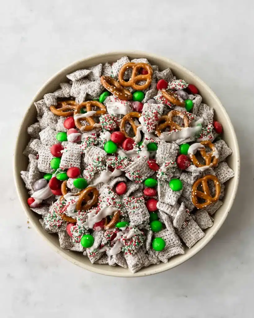 Christmas Puppy Chow (Festive Muddy Buddies) 1 Christmas Puppy Chow snack mix with M&M’s, pretzels, and powdered sugar in a white bowl