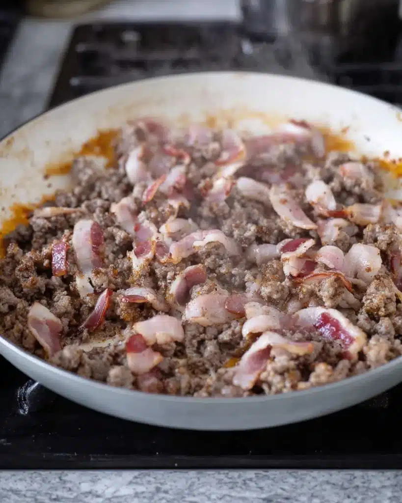Crack Breakfast Casserole 2 Bacon and sausage cooking together in skillet for Crack Breakfast Casserole