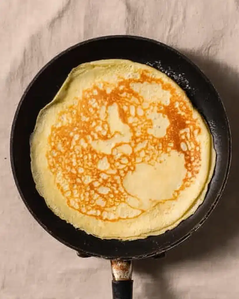 Crepes with Pancake Mix (Easy, Light & Delicious Breakfast Recipe) 4 Golden crepe cooking in a skillet for crepes with pancake mix