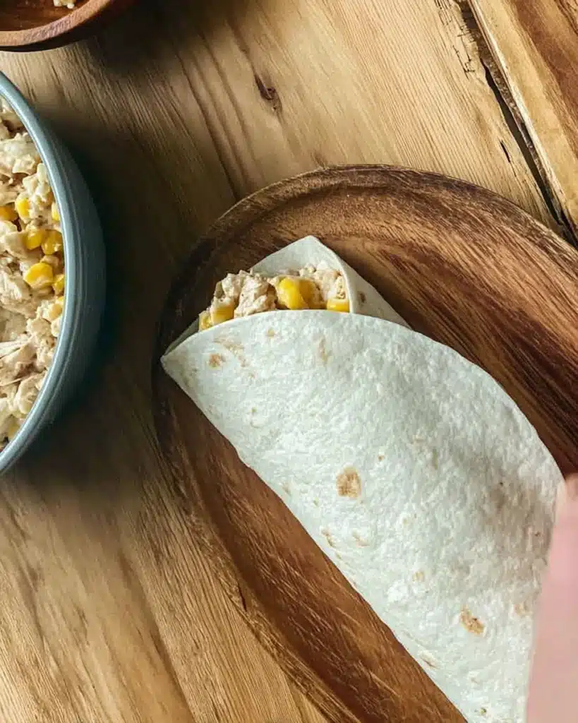 Easy Chicken Wraps (Quick & Flavorful Lunch Recipe) 4 Rolling a chicken wrap with creamy corn filling on wooden board