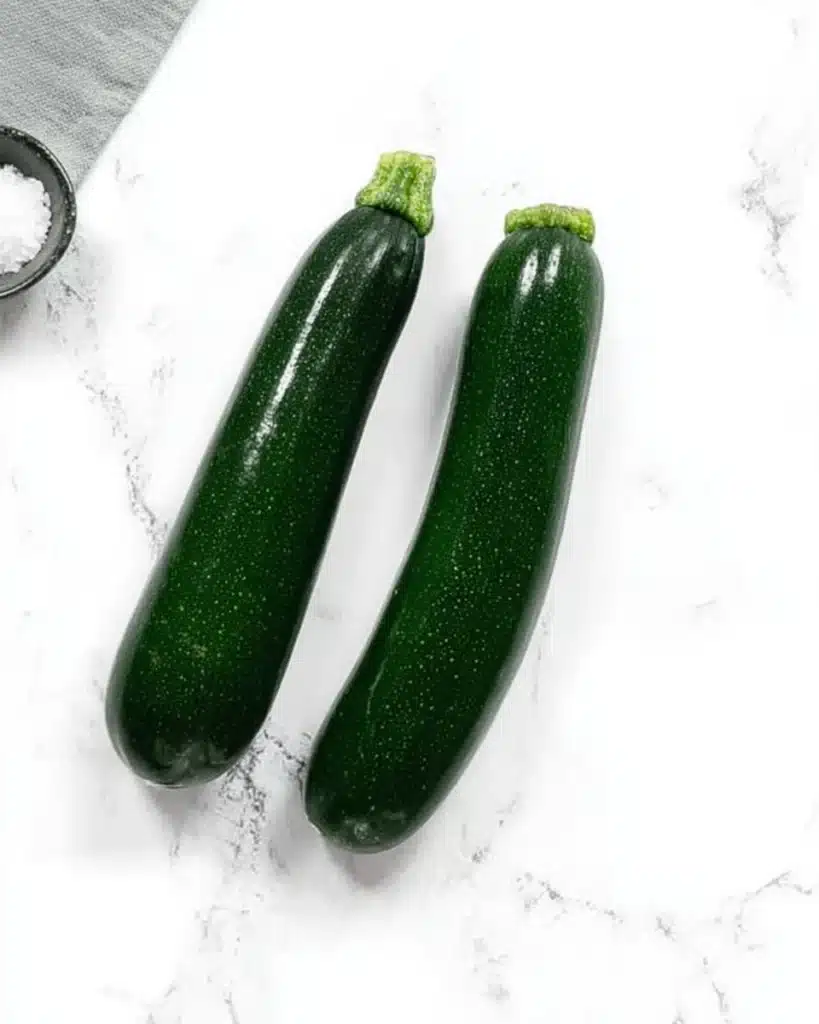 Greek Zucchini Tots (Crispy, Cheesy, and So Easy!) 2 Two fresh zucchinis and salt on a white marble surface