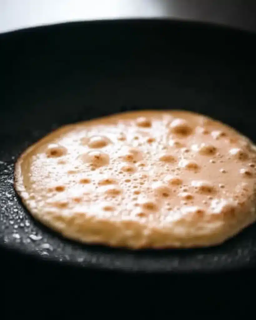 Pancakes – Fluffy, Quick, No-Fail 2 Pancake cooking in skillet with bubbles forming on surface
