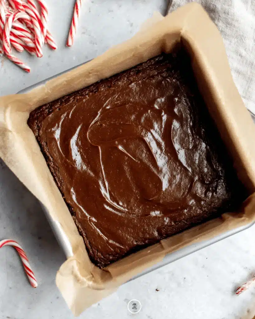 Chocolate brownie batter spread in parchment-lined square pan ready to bake