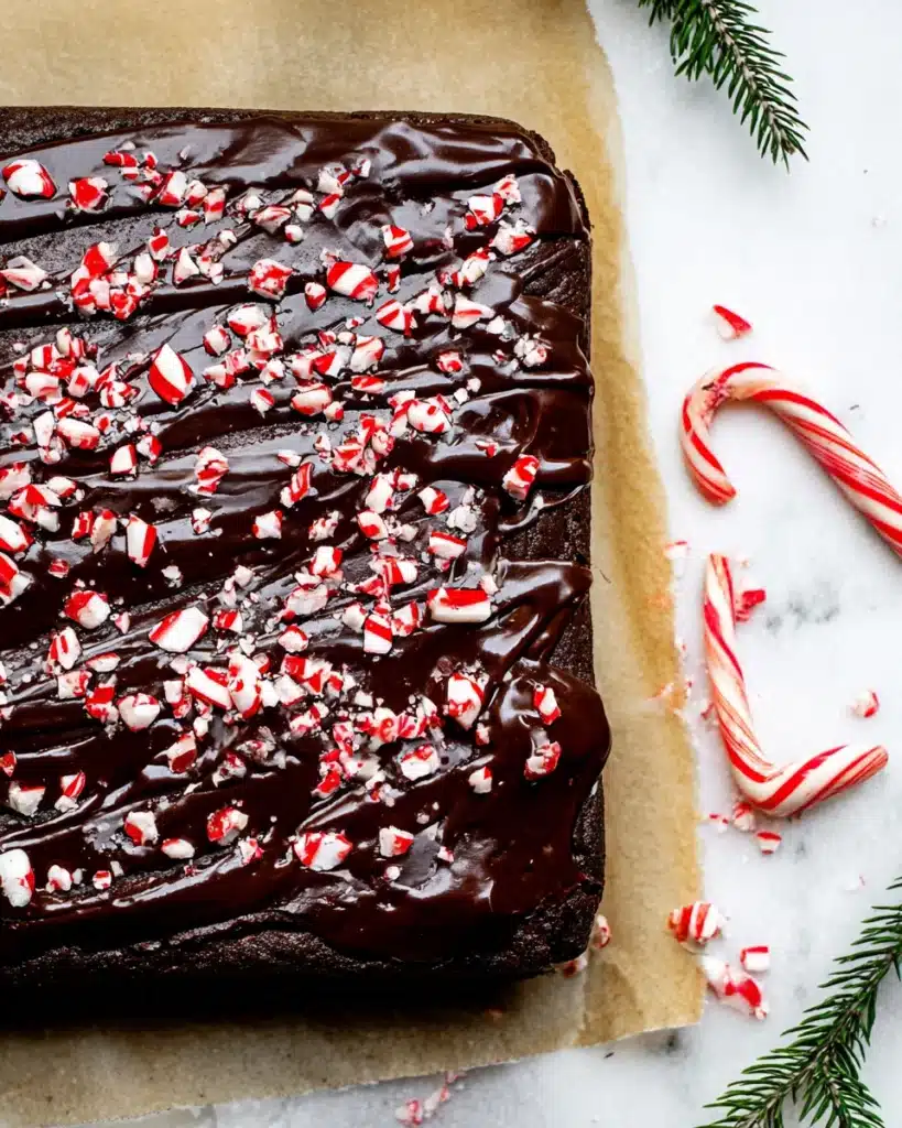 Pan of peppermint brownies topped with glossy chocolate ganache and crushed candy canes