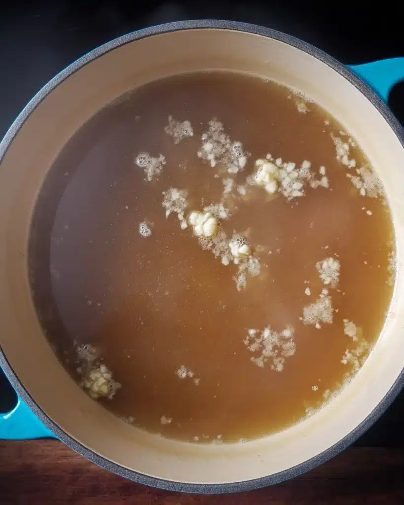 Quick & Easy Wonton Soup Recipe 2 Simmering wonton soup broth with garlic in a teal pot