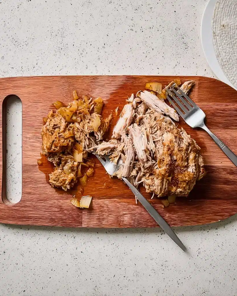 Shredded slow cooker Texas pulled pork on wooden cutting board with forks