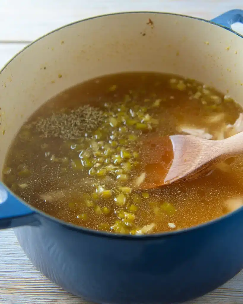 The Best White Chicken Chili (Creamy, Flavorful & Easy Recipe) 3 Chicken broth with green chilies and spices in a Dutch oven