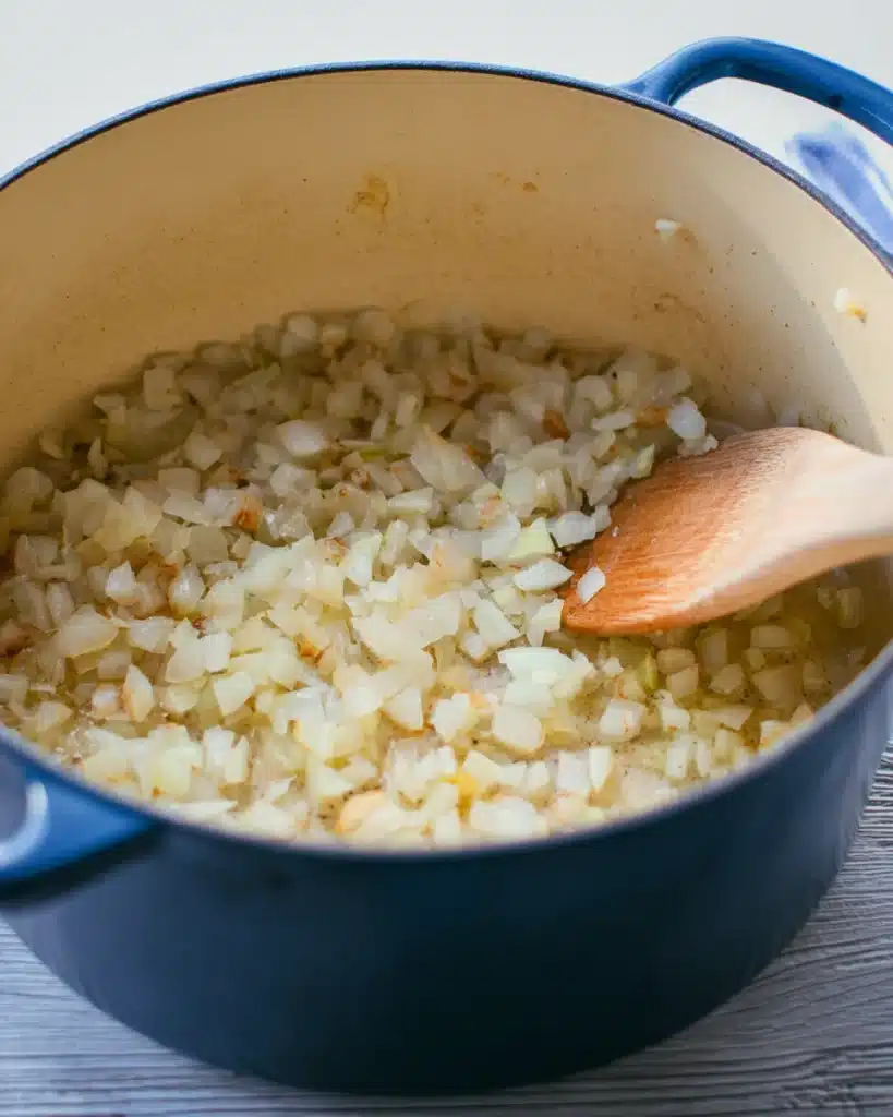 The Best White Chicken Chili (Creamy, Flavorful & Easy Recipe) 2 Sautéed onions in a Dutch oven with a wooden spoon