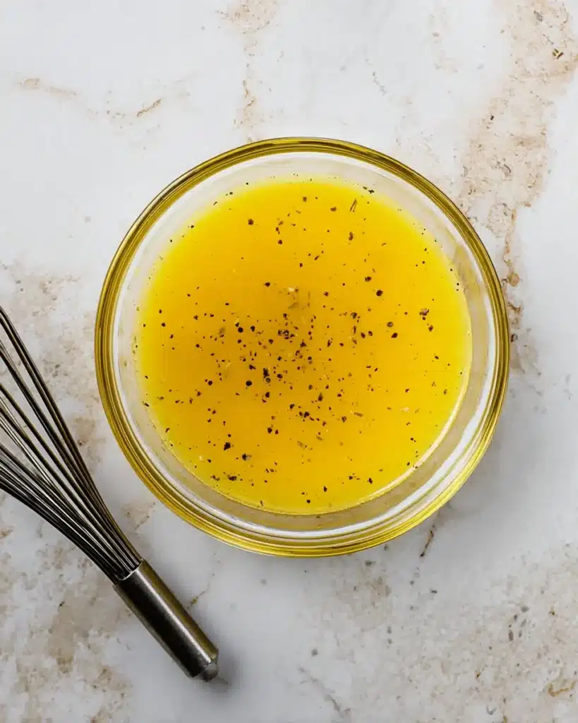 Lemon pepper butter sauce in glass bowl with whisk on marble surface