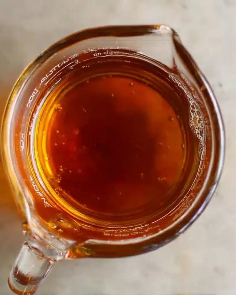 Almond Croissants 3 Glass cup of amber almond syrup on a stone countertop