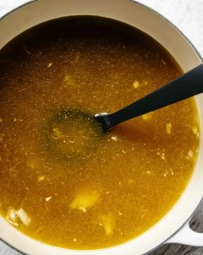 Avgolemono Soup (Greek Lemon Chicken & Rice Soup) 3 Golden chicken broth simmering for Avgolemono Soup in white pot