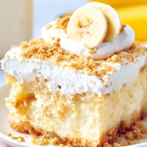 Slice of banana pudding poke cake with whipped topping and crushed cookies