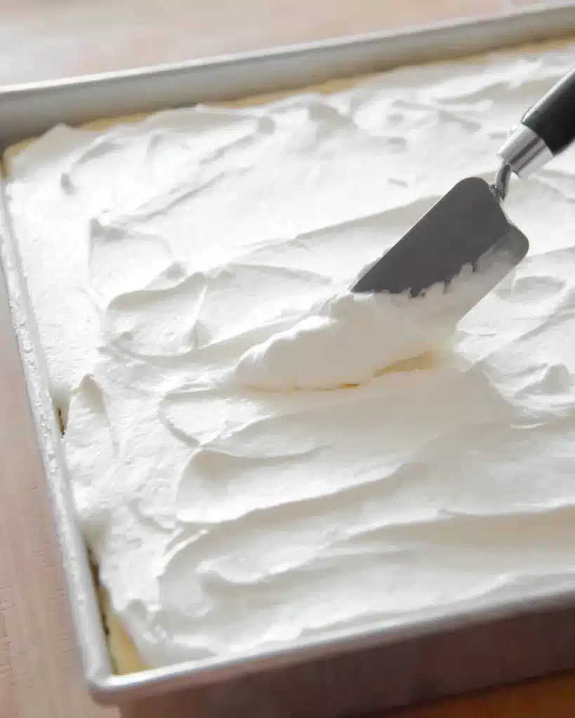 Spreading whipped topping over banana pudding poke cake