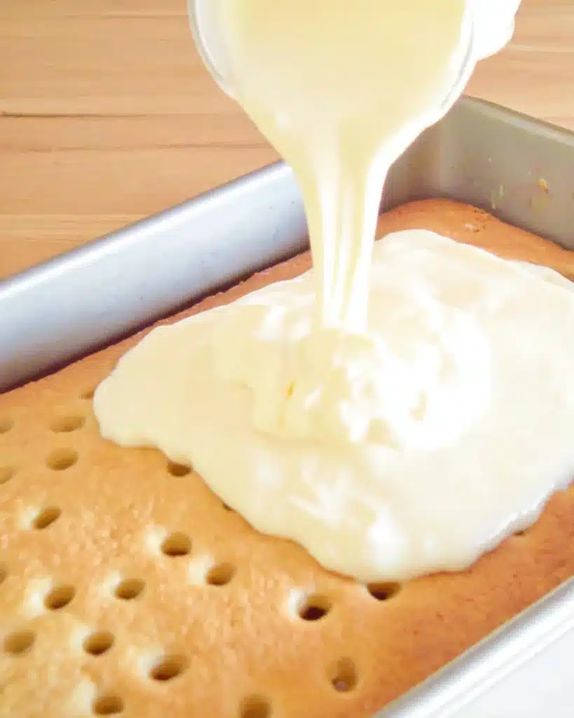 Pouring banana pudding over poke cake in baking pan