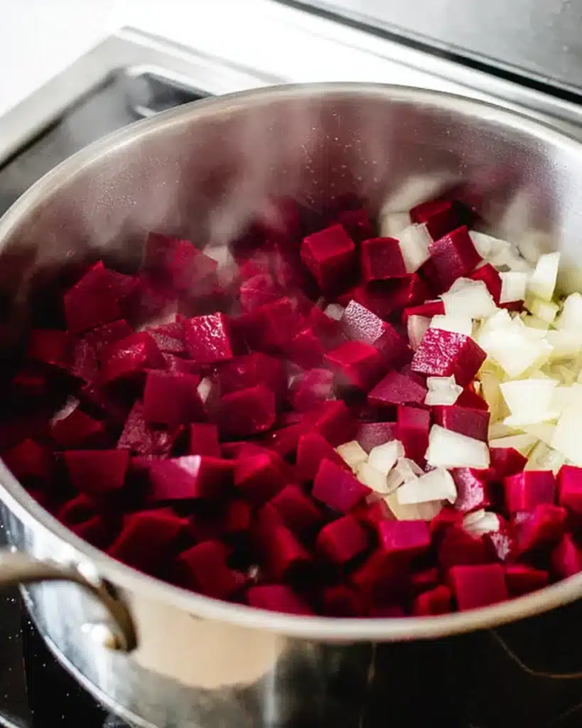 Diced beets and onions cooking in a stainless-steel pot
