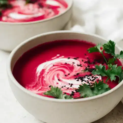 Smooth beet soup with coconut cream swirl and parsley garnish in white bowl