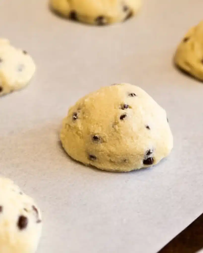 "Uncooked cannoli cookie dough scoops on a parchment paper-lined baking sheet."