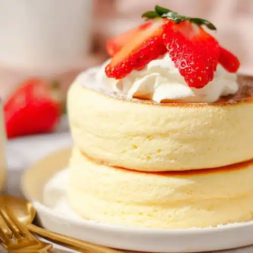 Fluffy Japanese soufflé pancakes topped with strawberries and whipped cream